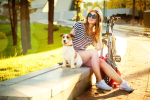 Smiling Hipster Girl with her Dog and Bike in the City. Toned and Filtered Photo with Bokeh and Copy Space. Urban Youth Lifestyle Concept.