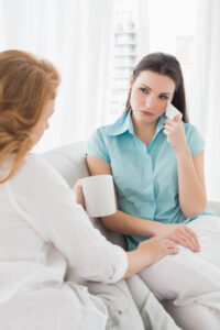 Young woman consoling a crying female friend while sitting on sofa at home